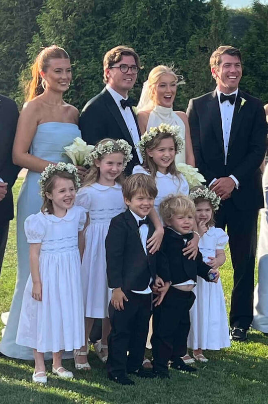 Bridal party with smiling flower girls in white dresses and page boys in black suits outdoors