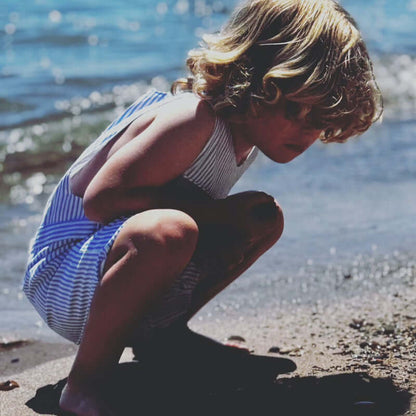 Child in a blue striped outfit playing on the beach, exploring the sandy shore near the water.