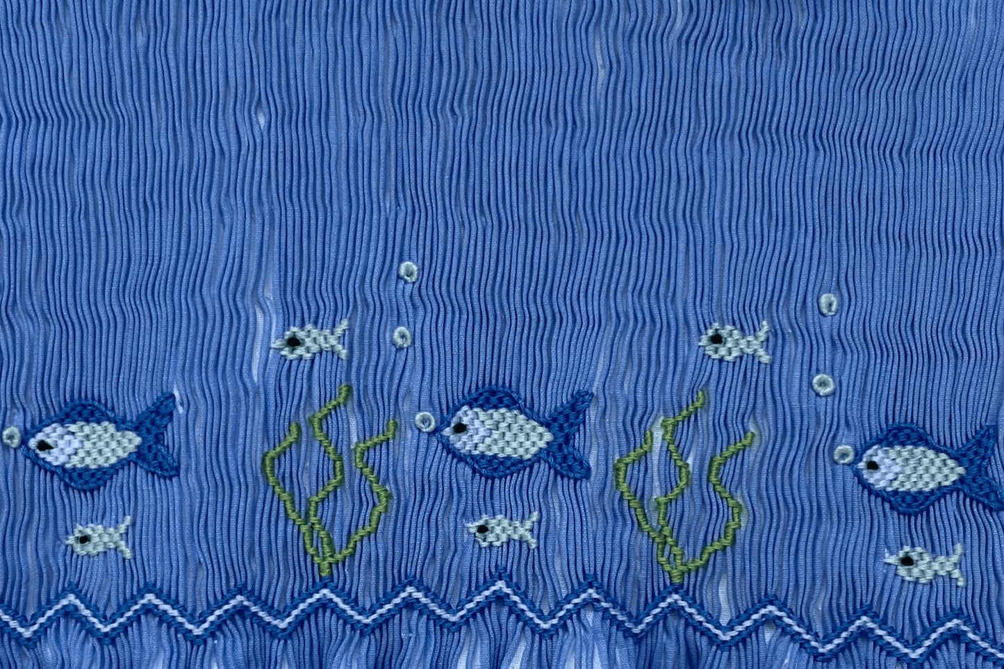 Smocked fish design on classic french blue stripe fabric, featuring playful under-the-sea scene with colorful fish and seaweed.