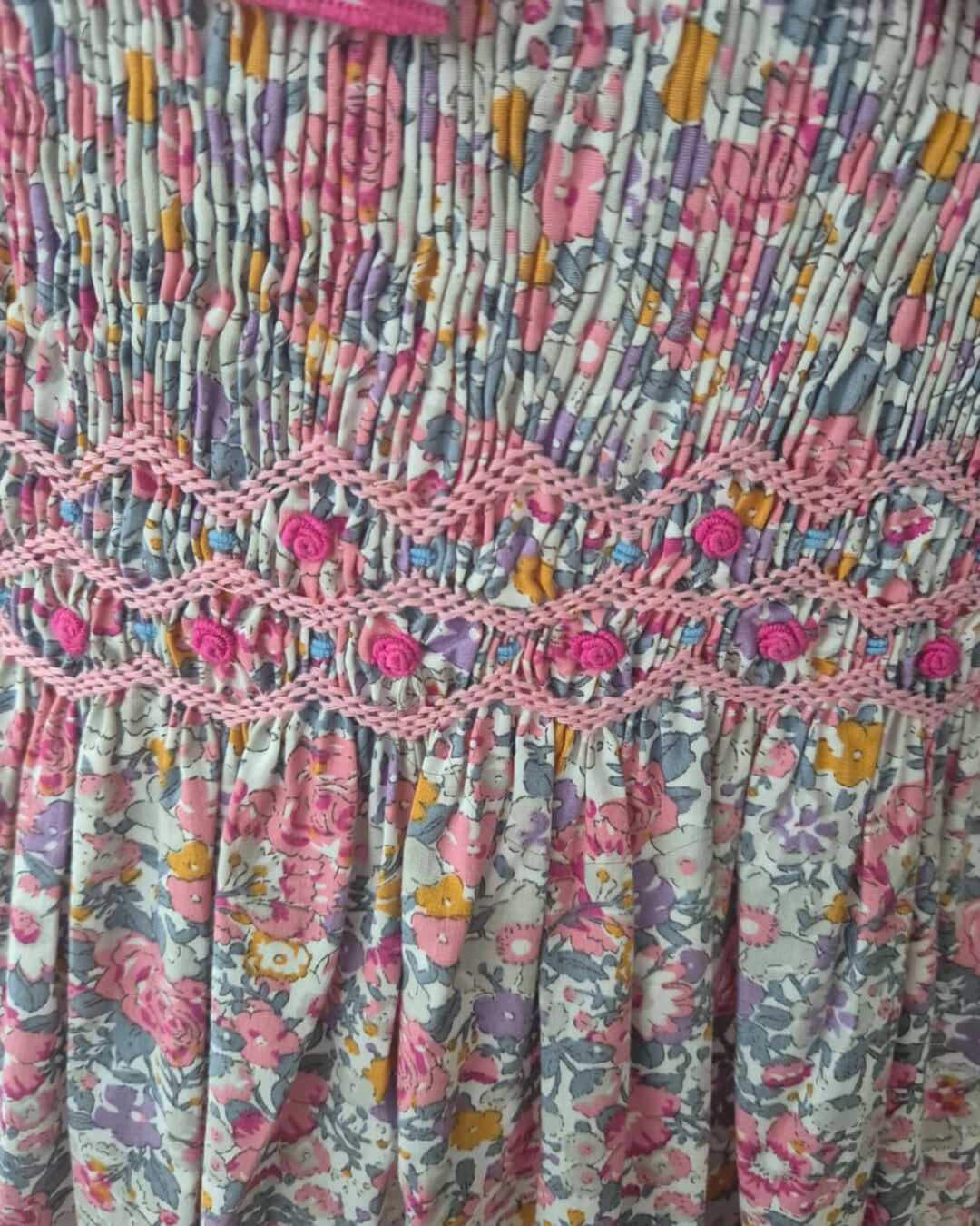 Close-up of hand-smocked floral dress featuring exquisite embroidery and ruffles in pastel colors.