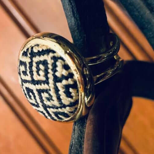 Black and gold Greek key needlepoint ring showcased on a dark surface, highlighting its unique design and adjustable bands.