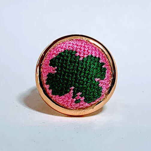 Pink Shamrock needlepoint ring on a light background, featuring a unique design with adjustable arms for versatile styling.