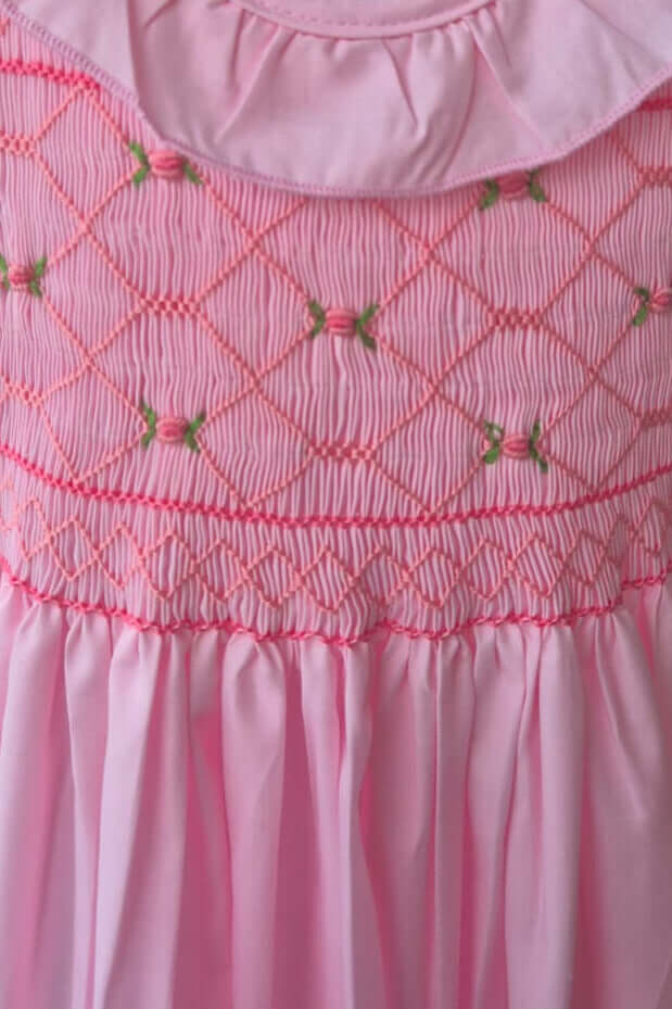 Close-up of pink hand-smocked ruffle dress with floral embroidery, perfect for special occasions.