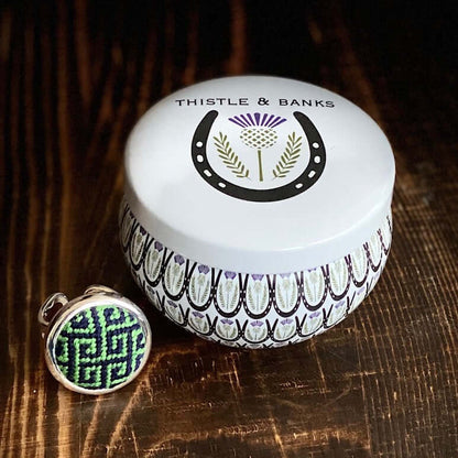 Thistle & Banks Navy & Kelly Greek Key Needlepoint Ring beside decorative storage jar on wooden surface.