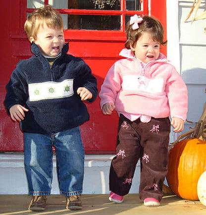 Kids wearing Smocked Turtle Polar Fleece Jackets with hand smocked turtle motifs, standing in front of a red door, smiling.